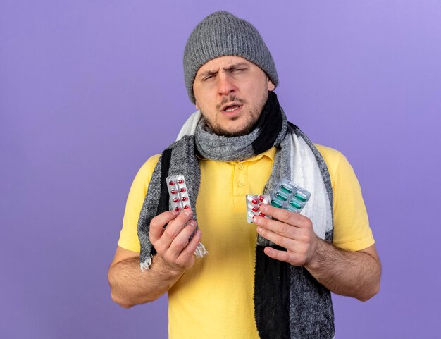 Unpleased young blonde ill slavic man wearing winter hat and scarf