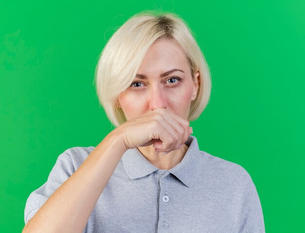 Unpleased young blonde ill slavic woman wipes nose with hand isolated on green wall with copy space