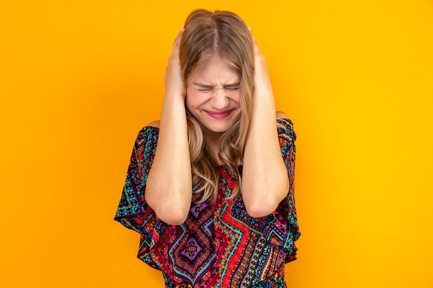 Unpleased young blonde slavic girl standing with closed eyes and holding her head