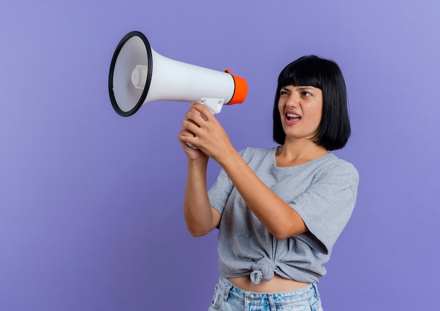 Unpleased young brunette caucasian girl holds and looks at loud speaker 