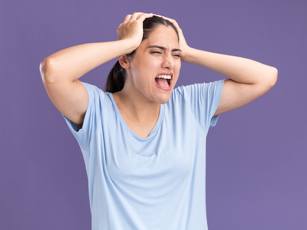 Unpleased young brunette caucasian girl puts hands on head on purple