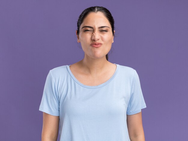 Unpleased young brunette caucasian girl standing with closed eyes on purple