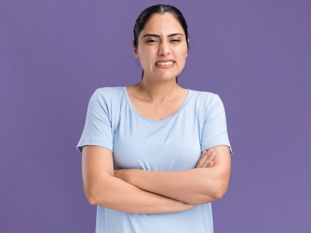 Unpleased young brunette caucasian girl standing with crossed arms isolated on purple wall with copy space