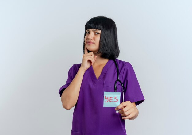 Недовольная молодая брюнетка женщина-врач в униформе со стетоскопом держит да