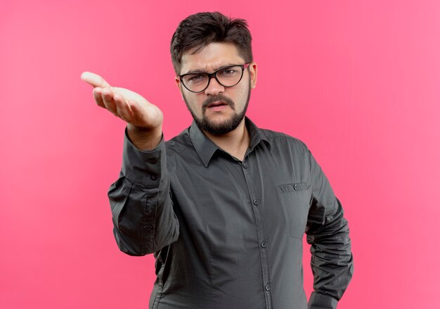 Free photo unpleased young businessman wearing glasses holding out hand to camera isolated on pink