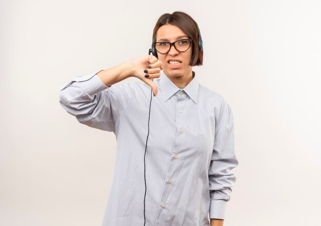 Unpleased young call center girl wearing glasses and headset showing thumb down isolated on white background with copy space