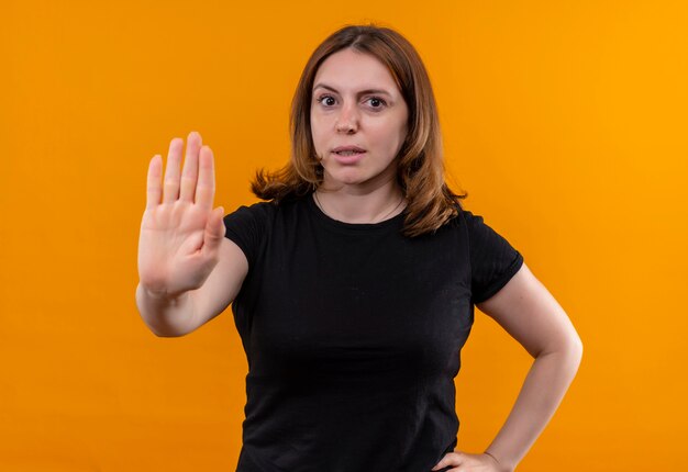 Unpleased young casual woman gesturing stop with hand on waist on isolated orange wall
