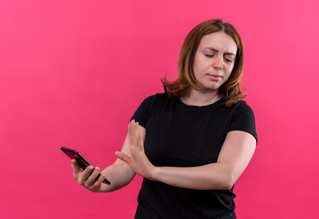 Unpleased young casual woman holding mobile phone and gesturing no on isolated pink wall