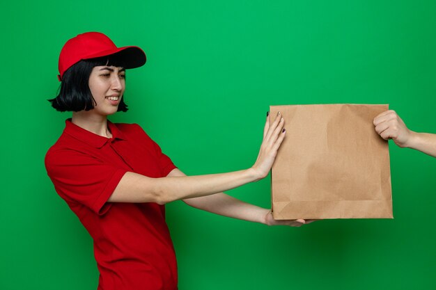 Unpleased young caucasian delivery girl giving paper food packaging to someone