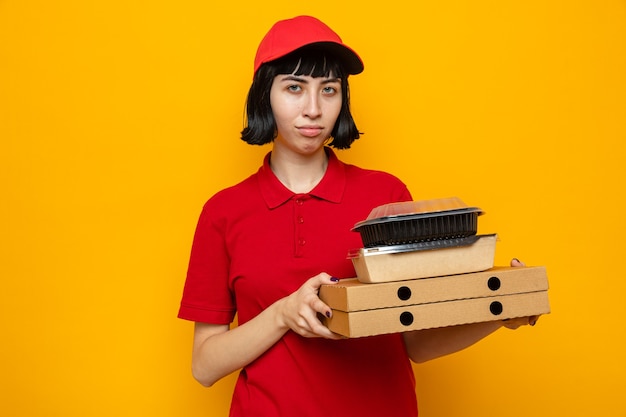 Unpleased young caucasian delivery girl holding food containers with packaging on pizza boxes