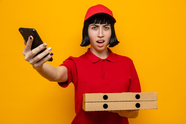 Недовольная молодая кавказская доставщица держит коробки для пиццы и телефон