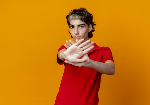 Unpleased young caucasian girl with pixie haircut gesturing no at camera isolated on orange background with copy space