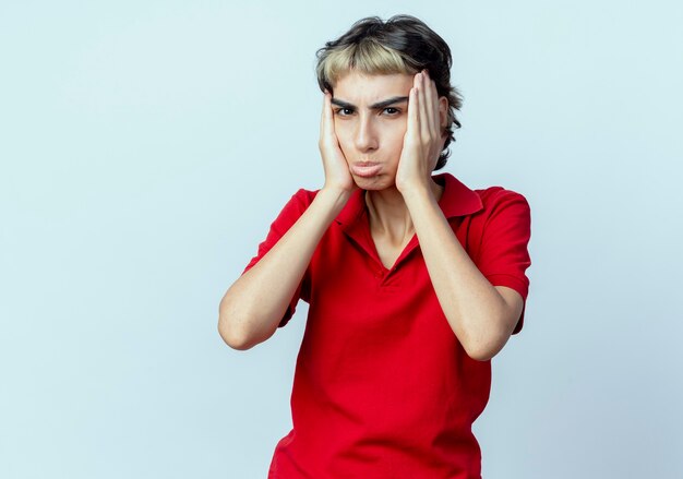 Unpleased young caucasian girl with pixie haircut putting hands on face isolated on white background with copy space