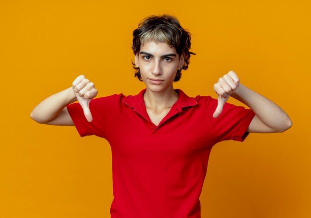 Unpleased young caucasian girl with pixie haircut showing thumbs down isolated on orange background