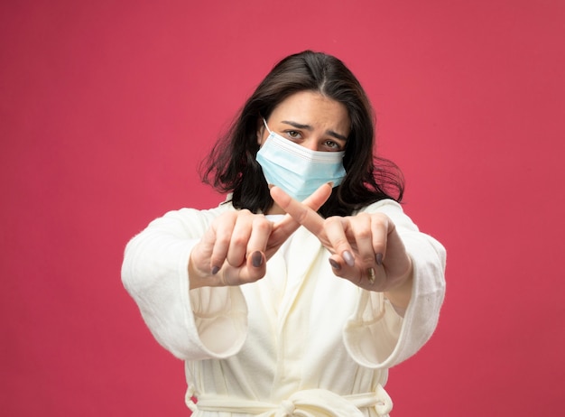 Foto gratuita giovane ragazza malata caucasica dispiaciuta che indossa veste e maschera che guarda l'obbiettivo che non fa alcun gesto isolato su priorità bassa cremisi