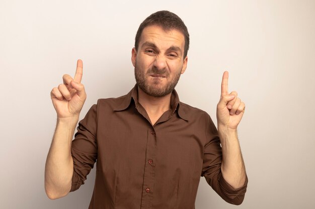 Unpleased young caucasian man looking at camera biting lip pointing up isolated on white background