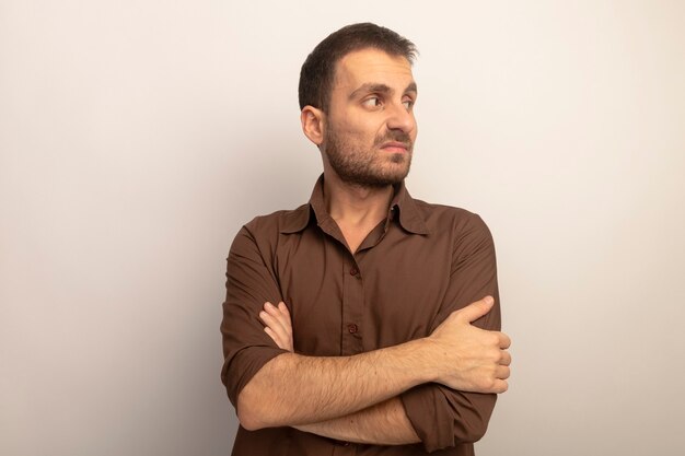 Unpleased young caucasian man standing with closed posture looking at side isolated on white background with copy space