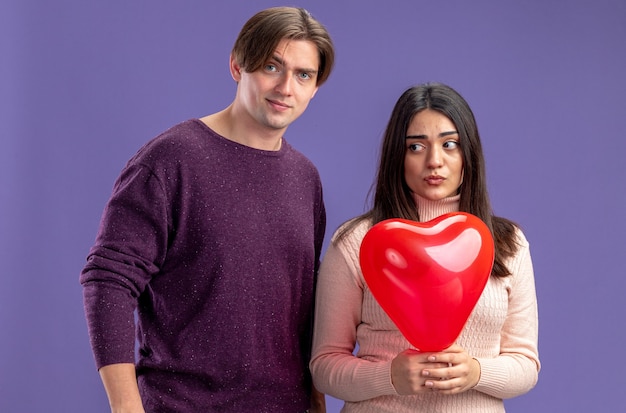 Unpleased young couple on valentines day girl holding heart balloon isolated on blue background