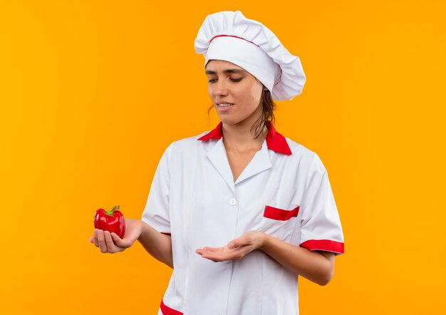 요리사 유니폼을 입고 손으로 토마토를 복사 공간으로 보여주는 불쾌한 젊은 여성 요리사