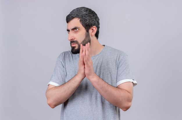 Unpleased young handsome caucasian man keeping hands together and looking at side isolated on white background with copy space