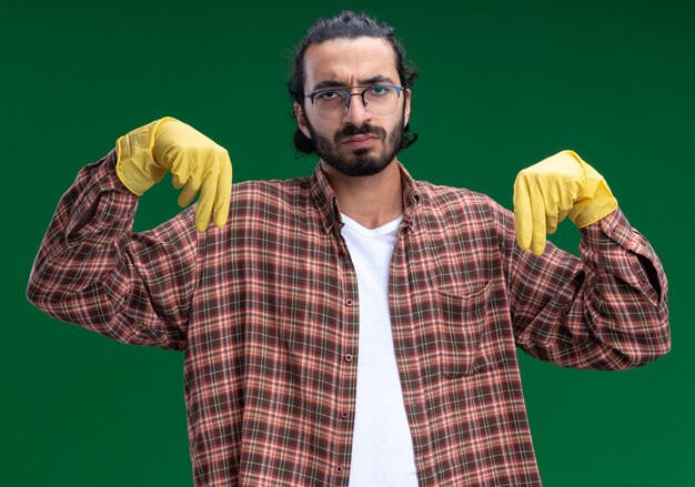 緑の壁に何かを持っているふりをして、Tシャツと手袋を着た不愉快な若いハンサムな掃除男