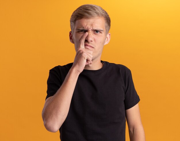 Unpleased young handsome guy wearing black shirt scratching nose isolated on yellow wall