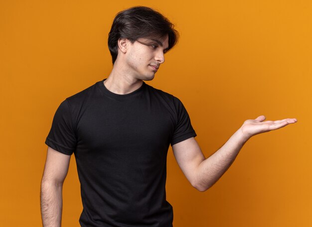 Unpleased young handsome guy wearing black t-shirt pretending holding something isolated on orange wall with copy space