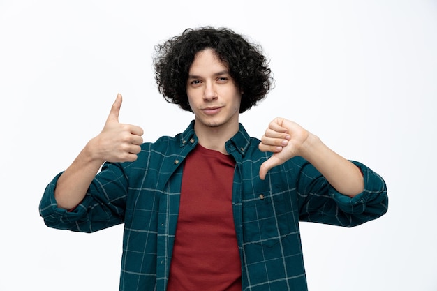 Unpleased young handsome man looking at camera showing thumbs up and down isolated on white background