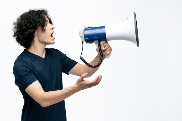 Unpleased young handsome man standing in profile view talking into speaker showing empty hand looking at side isolated on white background