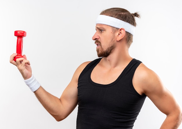 Foto gratuita il giovane sportivo bello dispiaciuto indossa la fascia e i braccialetti che tengono il manubrio e lo guarda isolato su uno spazio bianco