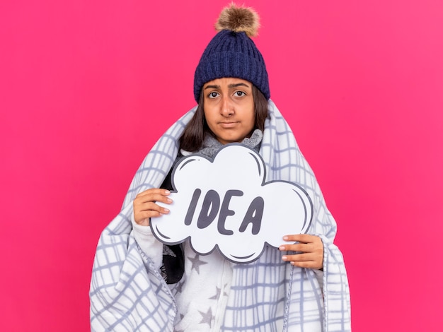 Foto gratuita giovane ragazza malata dispiaciuta che indossa il cappello invernale con sciarpa avvolta in plaid tenendo idea bolla isolata su sfondo rosa