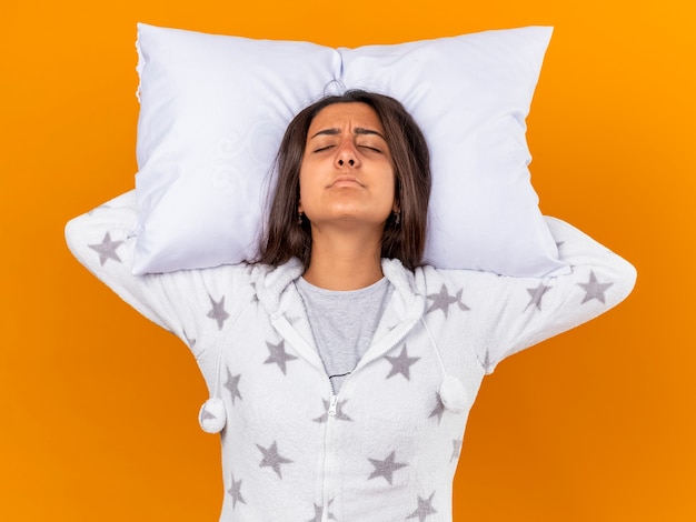 Free photo unpleased young ill girl with closed eyes hugging pillow holding pillow behind head isolated on yellow background