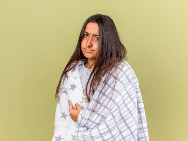Unpleased young ill girl wrapped in plaid points at side isolated on olive green background