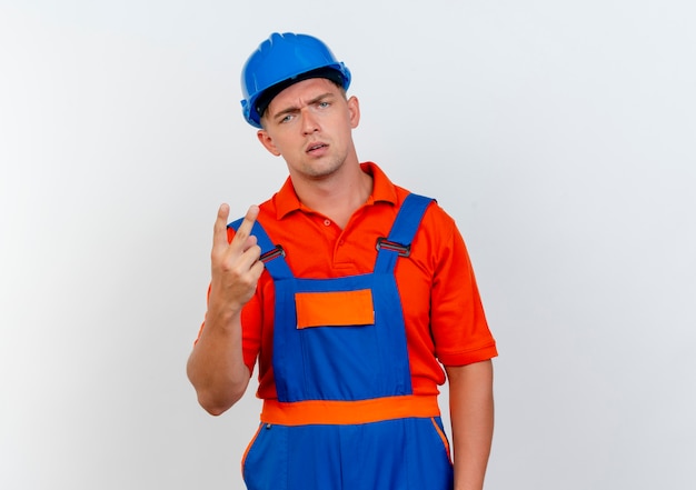 Unpleased young male builder wearing uniform and safety helmet showing two on white