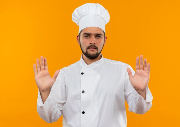 주황색 공간에 고립 된 빈 손을 보여주는 요리사 유니폼에 불쾌한 젊은 남성 요리사