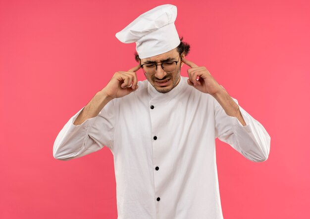 Free photo unpleased young male cook wearing chef uniform and glasses closed ears isolated on pink wall