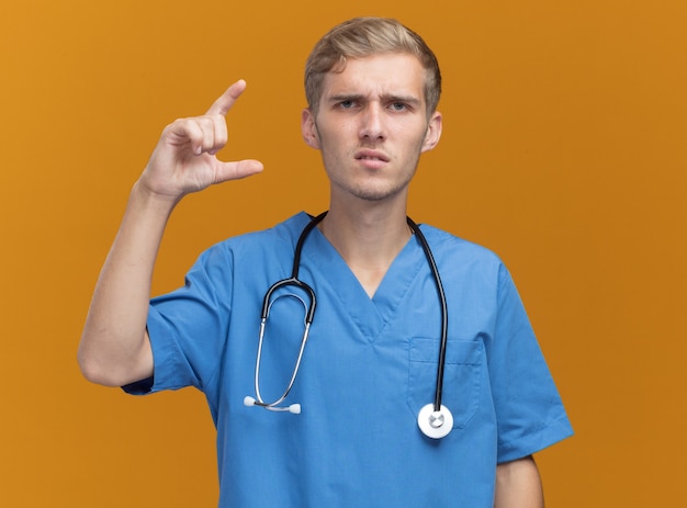 Free photo unpleased young male doctor wearing doctor uniform with stethoscope showing size isolated on orange wall