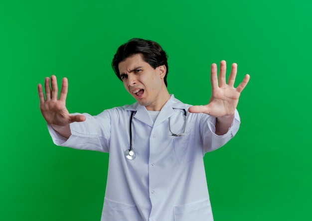 Unpleased young male doctor wearing medical robe and stethoscope looking doing no gesture isolated