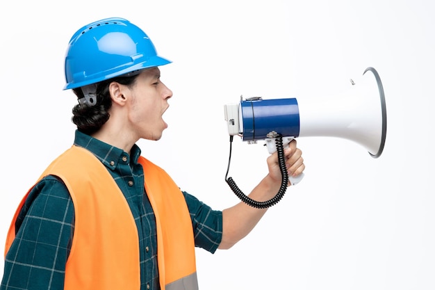 Free photo unpleased young male engineer wearing safety helmet and safety vest standing in profile view looking at side talking in loudspeaker isolated on white background