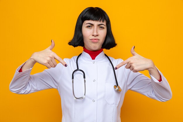 Недовольная молодая симпатичная кавказская девушка в униформе врача со стетоскопом, направленным вниз