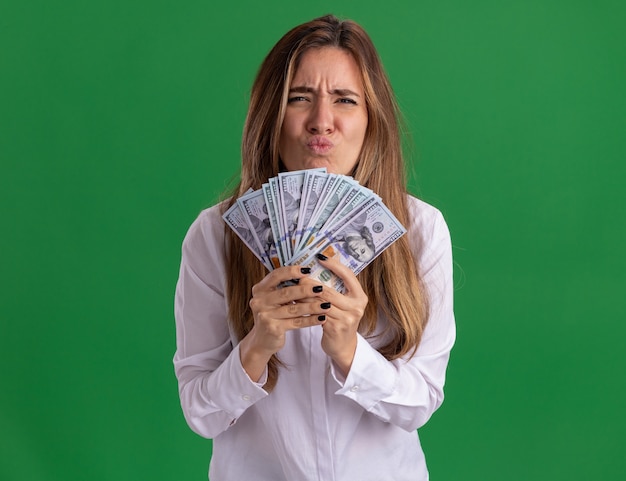 Unpleased young pretty caucasian girl holds money isolated on green wall with copy space