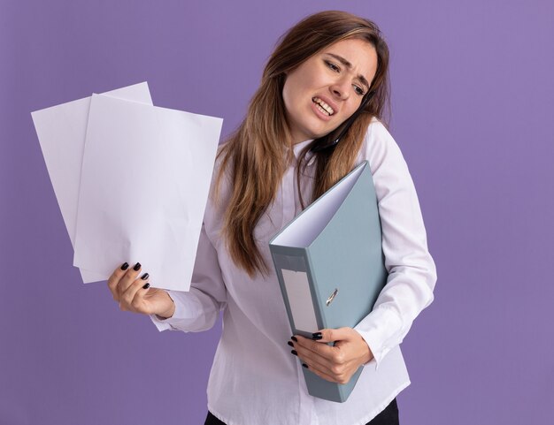 Unpleased young pretty caucasian girl holds paper sheets and file folder talking on phone isolated on purple wall with copy space