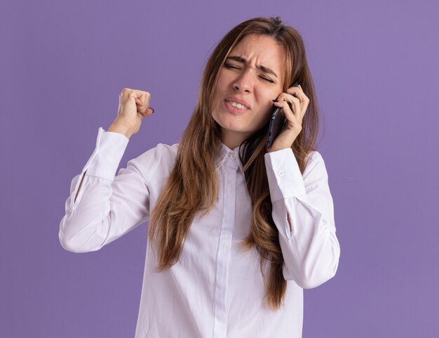 Unpleased young pretty caucasian girl keeps fist and talks on phone