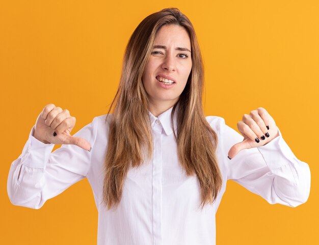 Unpleased young pretty caucasian girl thumbs down with two hands on orange 