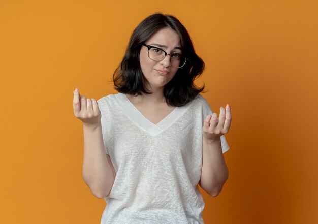 Unpleased young pretty caucasian girl wearing glasses doing money gesture at camera isolated on orange background with copy space