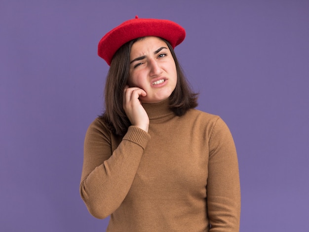 Unpleased young pretty caucasian girl with beret hat puts hand on face