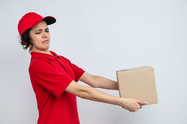 Unpleased young pretty delivery woman holding cardboard box 