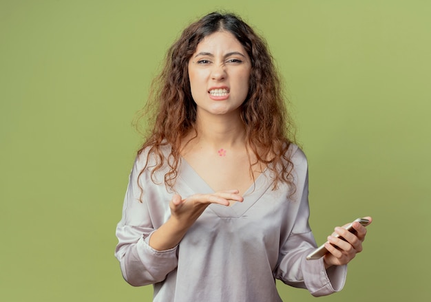 Soddisfatto giovane bella femmina lavoratore di ufficio azienda e punti con la mano al telefono isolato sulla parete verde oliva