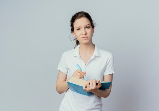 Unpleased young pretty female student holding open book and pen isolated on white background with copy space