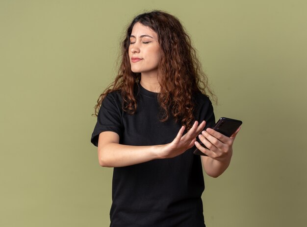 Unpleased young pretty woman holding mobile phone doing refusal gesture with closed eyes